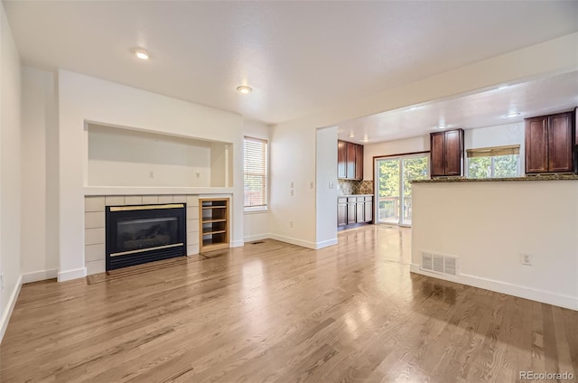 unfurnished living room featuring light wood-type flooring and a tiled fireplace