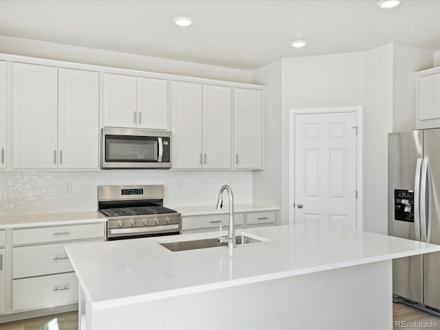 kitchen with appliances with stainless steel finishes, sink, white cabinets, and an island with sink