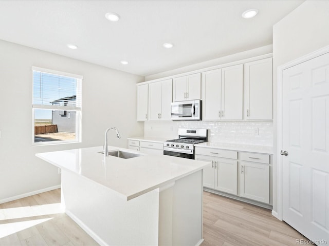 kitchen with white cabinetry, stainless steel appliances, an island with sink, light hardwood / wood-style floors, and sink