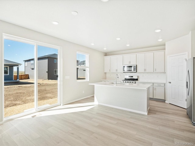 kitchen with white cabinetry, stainless steel appliances, backsplash, light hardwood / wood-style flooring, and a center island with sink