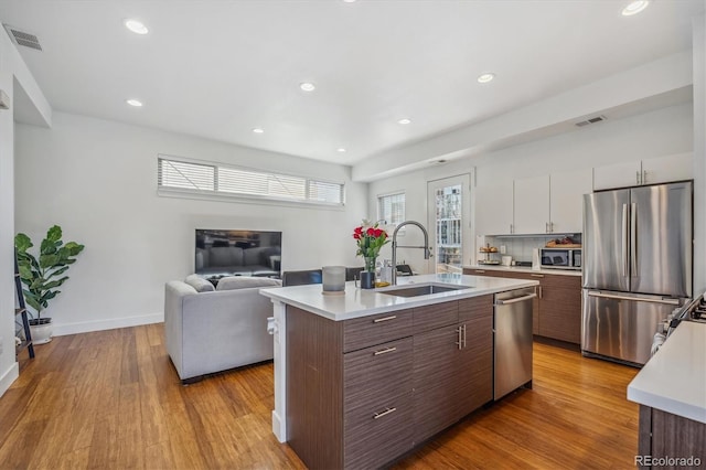 kitchen with appliances with stainless steel finishes, an island with sink, dark brown cabinetry, sink, and white cabinetry