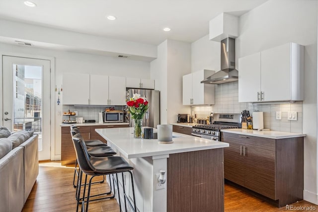 kitchen with wall chimney range hood, stainless steel appliances, a breakfast bar area, light countertops, and decorative backsplash