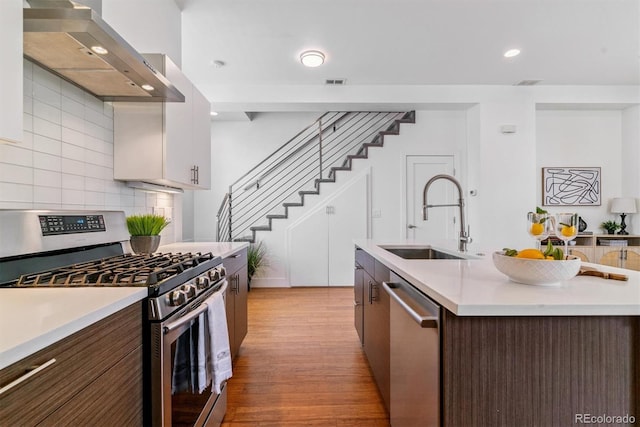 1216 Perry St, Denver, CO 80204 - kitchen with stainless steel appliances, wall chimney exhaust hood, light countertops, light wood-style flooring, and decorative backsplash