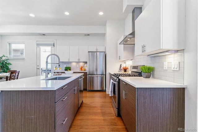 1216 Perry St, Denver, CO 80204 - kitchen with stainless steel appliances, wall chimney exhaust hood, light wood finished floors, an island with sink, and light countertops