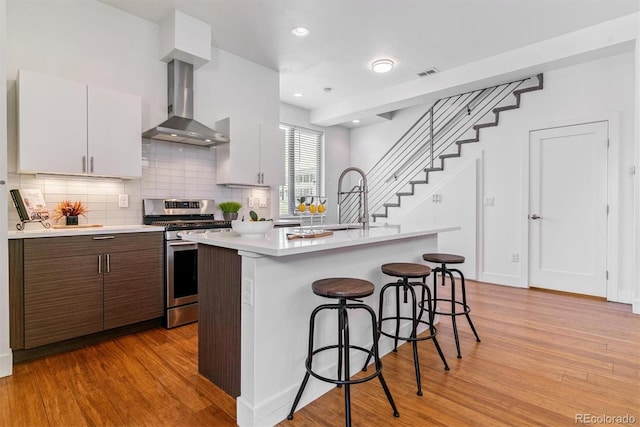 1216 Perry St, Denver, CO 80204 - kitchen with stainless steel range with gas cooktop, wall chimney range hood, light wood-type flooring, light countertops, and a kitchen bar