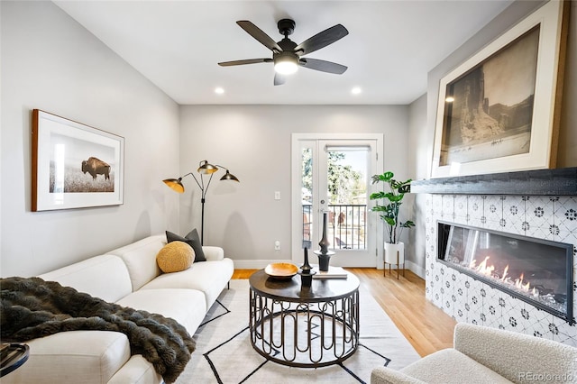 living room with light wood-type flooring, ceiling fan, and a tile fireplace