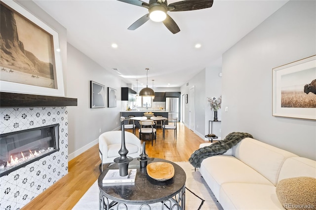 living area with baseboards, light wood finished floors, recessed lighting, a tile fireplace, and ceiling fan