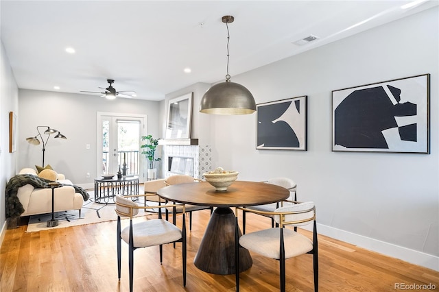 dining area featuring visible vents, light wood finished floors, baseboards, ceiling fan, and a tile fireplace