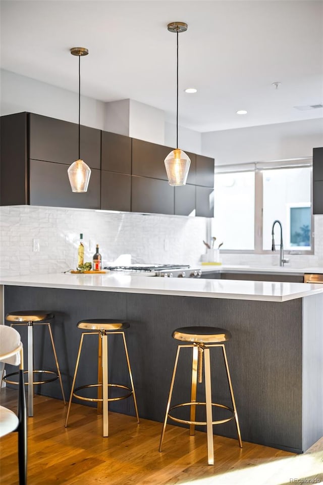 kitchen featuring light wood finished floors, backsplash, pendant lighting, a breakfast bar, and modern cabinets