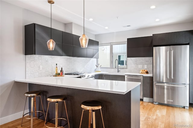 kitchen featuring a breakfast bar area, stainless steel appliances, light countertops, light wood-style floors, and modern cabinets