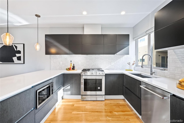 kitchen featuring modern cabinets, a sink, light wood-style floors, appliances with stainless steel finishes, and hanging light fixtures