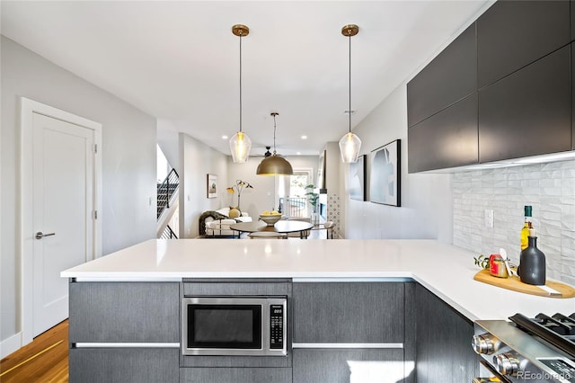 kitchen featuring wood finished floors, a peninsula, light countertops, stainless steel microwave, and backsplash