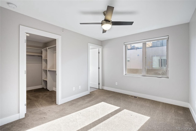 unfurnished bedroom with a walk in closet, carpet, baseboards, ceiling fan, and a closet