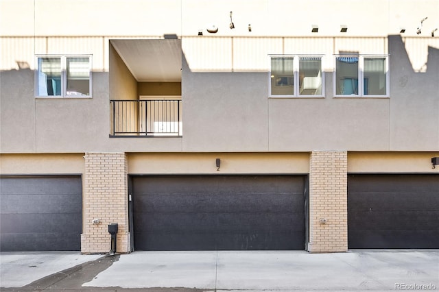 exterior space with brick siding, a balcony, a garage, and stucco siding