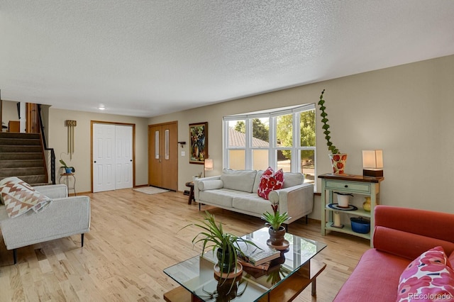 living area featuring light wood-style floors, a textured ceiling, and stairs