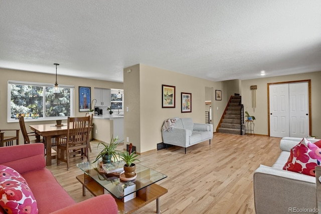 living area featuring stairway, light wood finished floors, and a textured ceiling