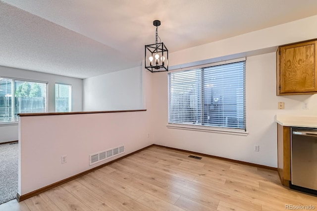 unfurnished dining area featuring baseboards, light wood-style flooring, a chandelier, and visible vents