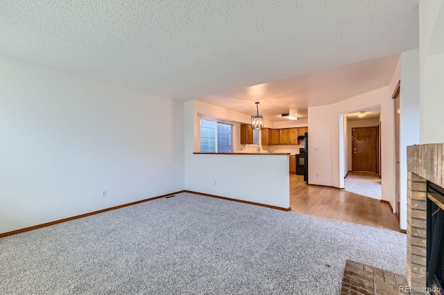 unfurnished living room with light colored carpet, a textured ceiling, baseboards, and a brick fireplace