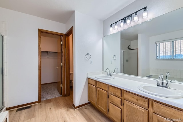 bathroom featuring a sink, double vanity, a stall shower, and wood finished floors