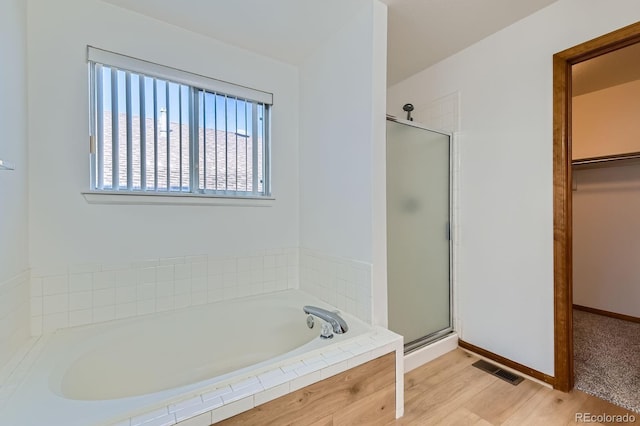 full bathroom featuring visible vents, wood finished floors, a walk in closet, a bath, and a shower stall