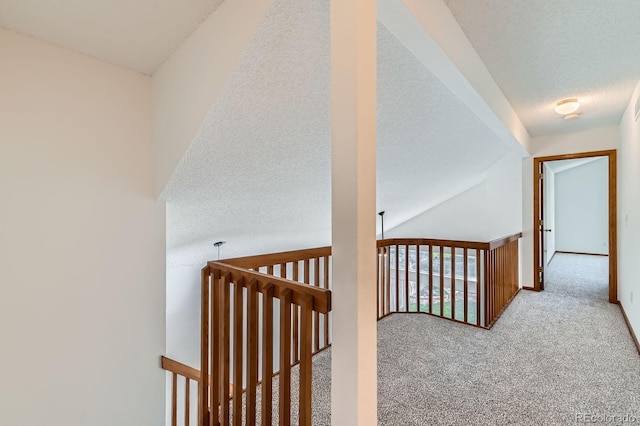 corridor featuring carpet flooring, a textured ceiling, and an upstairs landing