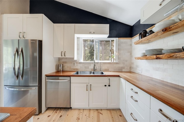 kitchen featuring light wood-style flooring, stainless steel appliances, a sink, vaulted ceiling, and wooden counters