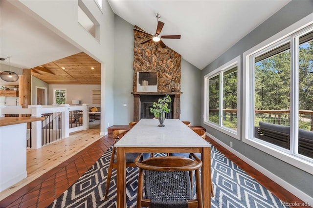 dining space with high vaulted ceiling, baseboards, and a stone fireplace