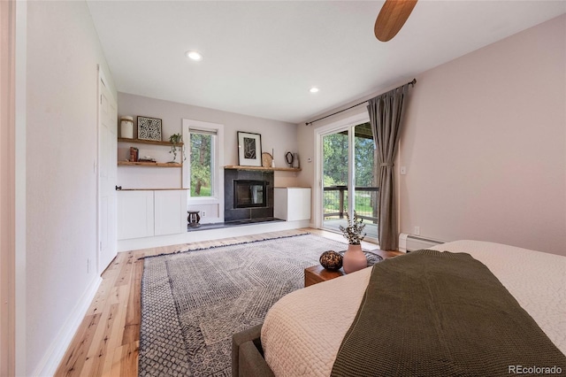 bedroom featuring a glass covered fireplace, access to outside, light wood-type flooring, a baseboard heating unit, and recessed lighting