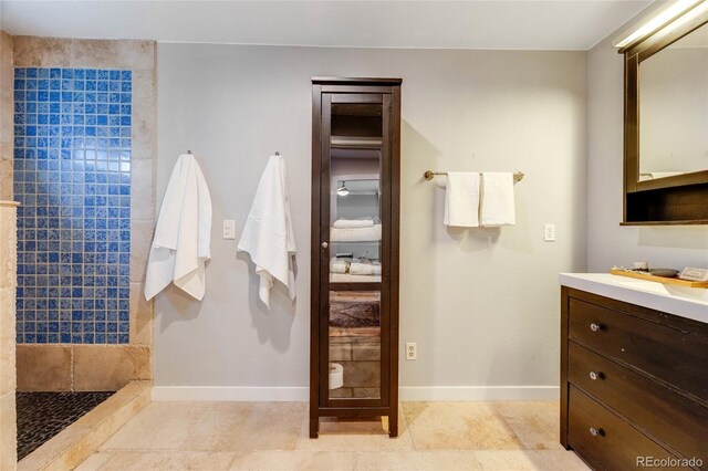 bathroom with tiled shower, vanity, and baseboards