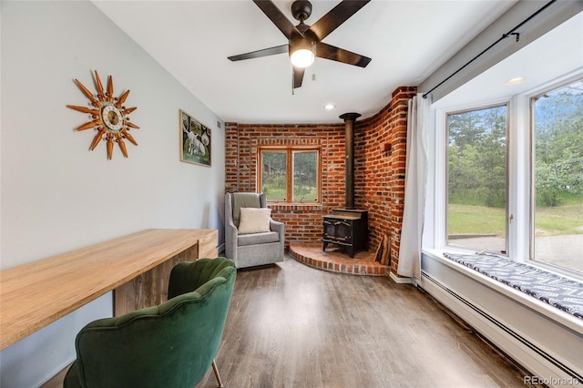 living area featuring a baseboard radiator, a wood stove, a healthy amount of sunlight, and wood finished floors