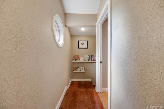 hallway with baseboards, wood finished floors, and a textured wall