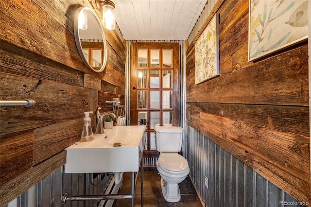 bathroom with a sink, wood walls, toilet, and tile patterned floors