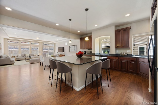 kitchen with hanging light fixtures, a kitchen island, dark wood-type flooring, a breakfast bar, and black refrigerator