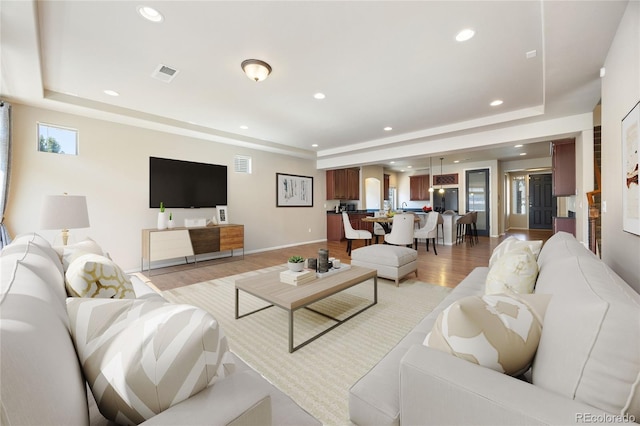 living room featuring a raised ceiling and light hardwood / wood-style floors