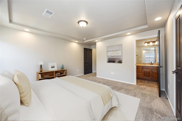 bedroom featuring a tray ceiling, sink, light carpet, and ensuite bathroom