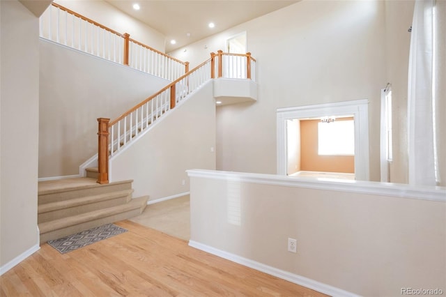 stairs with recessed lighting, baseboards, a high ceiling, and wood finished floors