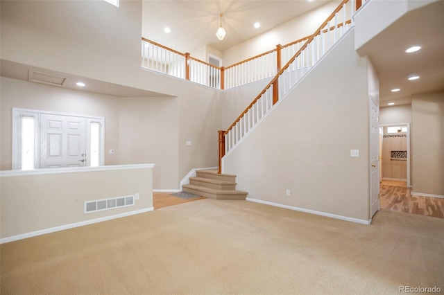 unfurnished living room featuring visible vents, recessed lighting, carpet floors, a high ceiling, and baseboards