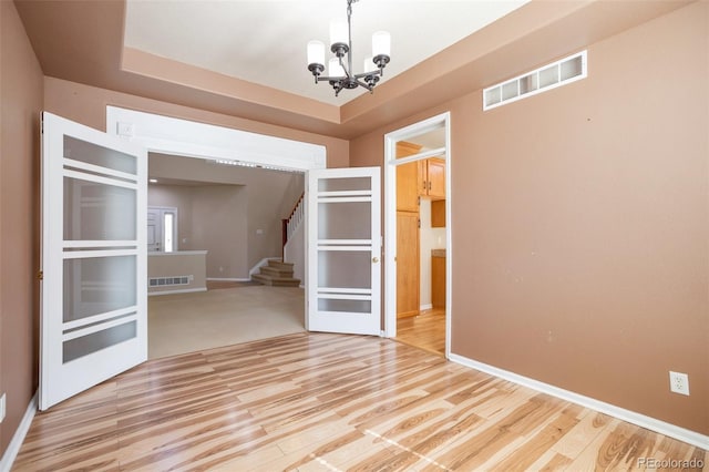 empty room featuring a notable chandelier, visible vents, light wood-style flooring, and stairway