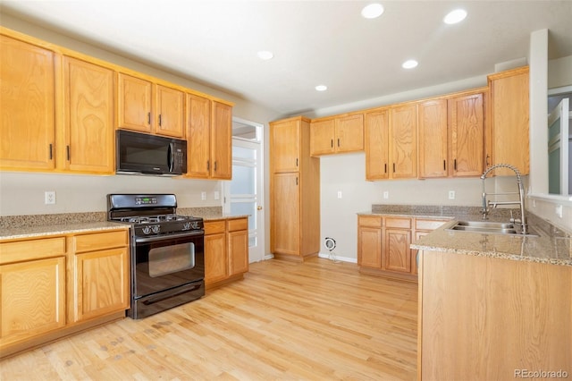 kitchen with a sink, light stone countertops, light wood-style floors, and black appliances