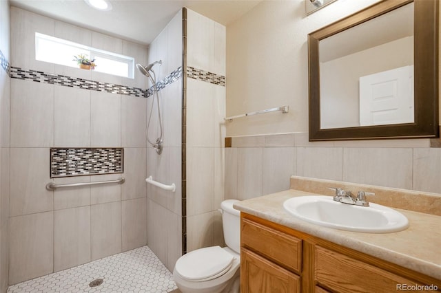 bathroom with tile walls, a wainscoted wall, toilet, a tile shower, and vanity