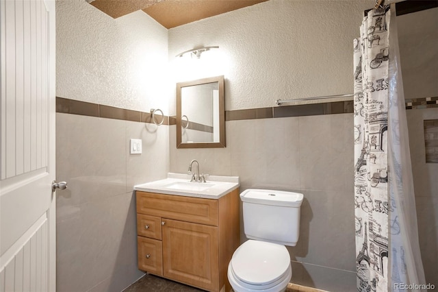 full bath with vanity, tile walls, toilet, and a textured wall