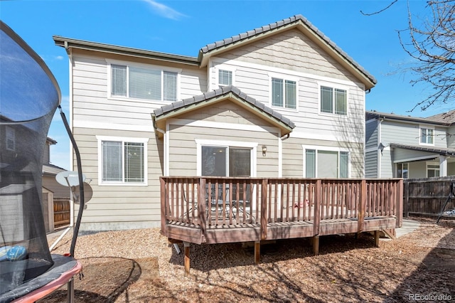 rear view of property featuring a deck, a trampoline, and fence