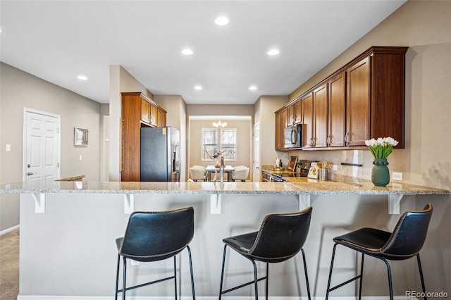 kitchen with a breakfast bar, light stone counters, appliances with stainless steel finishes, kitchen peninsula, and a notable chandelier