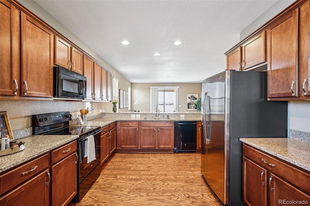 kitchen featuring light stone countertops, sink, light wood-type flooring, and black appliances