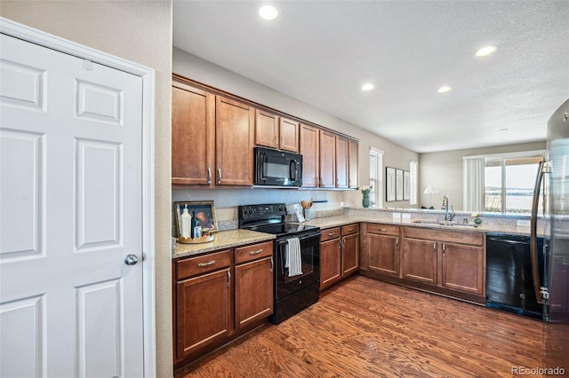 kitchen with light stone counters, dark wood-type flooring, sink, and black appliances