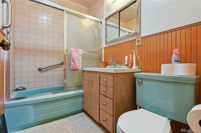 full bath featuring vanity, shower / bath combination with glass door, wood walls, wainscoting, and toilet