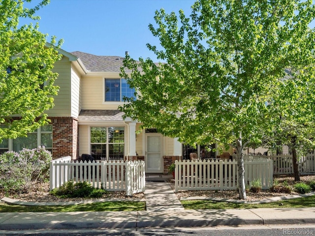 view of property hidden behind natural elements with brick siding, roof with shingles, and a fenced front yard