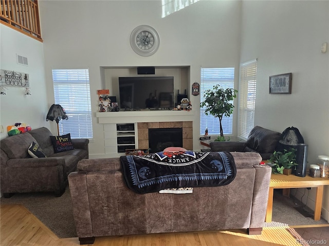 living room featuring a tiled fireplace, a towering ceiling, and hardwood / wood-style flooring