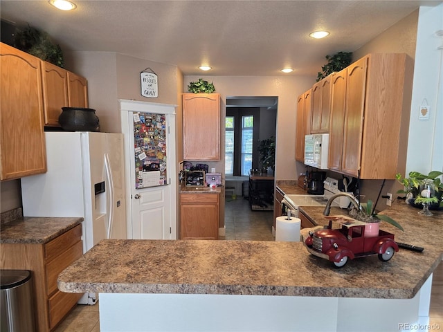 kitchen with kitchen peninsula, light tile patterned floors, white appliances, and a textured ceiling