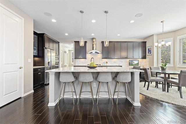 6728 S Catawba Way, Aurora, CO 80016 - kitchen featuring wall chimney exhaust hood, recessed lighting, decorative backsplash, a chandelier, and a center island with sink